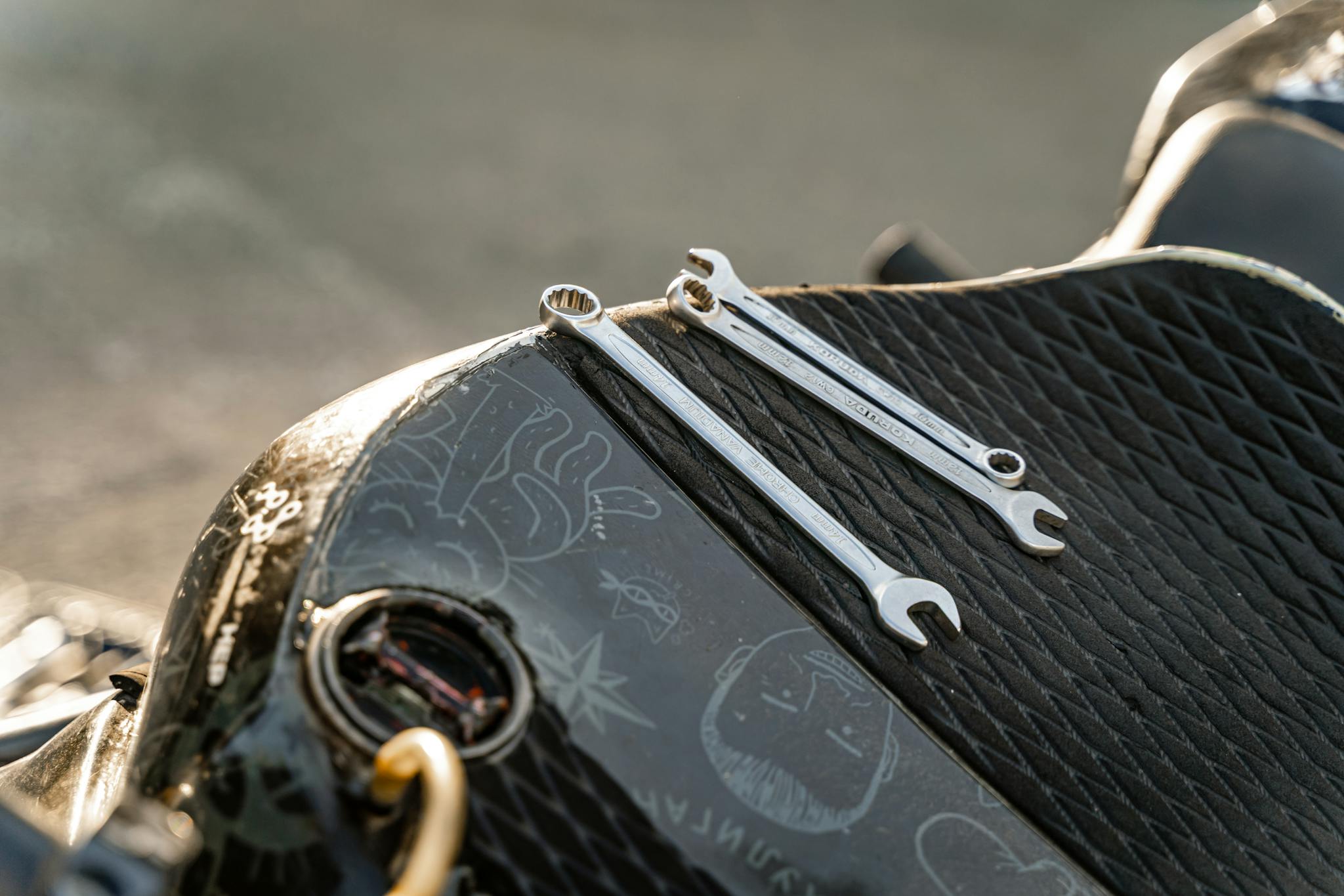 Close-up of a motorcycle seat with two wrenches, highlighting the tool setup in sunlight.